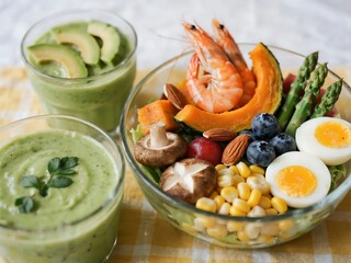 A vibrant bowl loaded with shrimp, roasted pumpkin, boiled eggs, corn, almonds, blueberries, mushrooms, and asparagus, paired with a creamy avocado smoothie