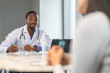 African doctor showing knee joint X-ray on tablet and bone model with patient, orthopedic...