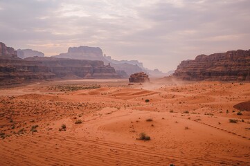 Fototapeta premium Scenic panorama of a sandy valley with dusty paths and rocky formations under a sandstorm effect.