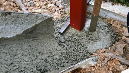 A builder pours a wet concrete from a mixer truck into a foundation. Pouring cement into pit with pillar. Foundational work. Workers control a mix flows through the gutter. Building industry.