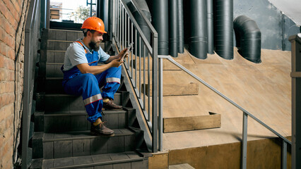 Technician using tablet on industrial staircase during break. Concept of HR and recruitment, modern workforce, motivation, and professional lifestyle visuals.