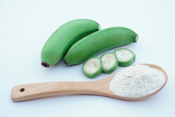 Green bananas and banana flour on wooden spoon, natural gluten-free alternative rich in resistant starch, popular in healthy diets, organic food products, and functional nutrition.