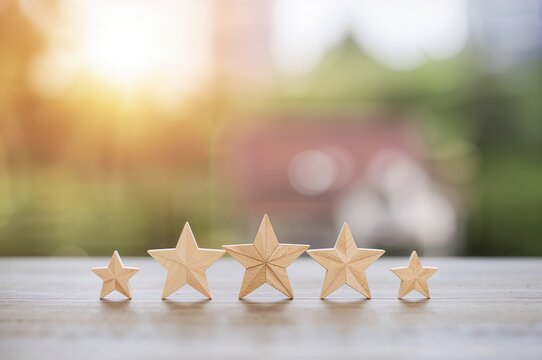 Five star ratings placed beside a house model on a wooden surface with a natural blurred backdrop, symbolizing top-tier quality and excellence in property reviews. - Powered by Adobe