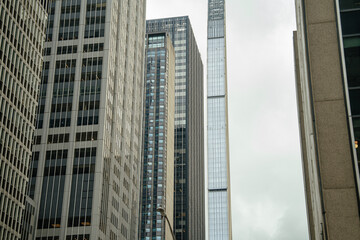 Obraz premium A group of modern skyscrapers rises high into the cloudy sky in Midtown Manhattan, New York City. The tall glass and steel buildings reflect the architectural power of the urban landscape.