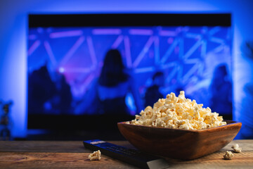 A wooden bowl of popcorn and remote control in the background the TV works. Evening cozy watching a movie or TV series at home