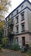 Naklejka premium Old Building in Autumn: An aged multi-story structure stands proudly amidst a vibrant autumn scene, exhibiting its historic architecture with a touch of nature's embrace.