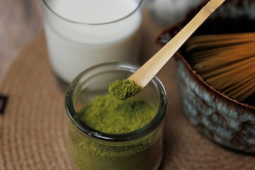 A wooden spoon holds a scoop of bright green matcha powder over a glass container filled with more powder.