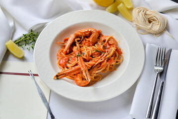 pasta with scampi in a white plate on a light background with lemon and cutlery