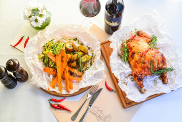whole baked chicken on the table with grilled vegetables and red wine in a bottle