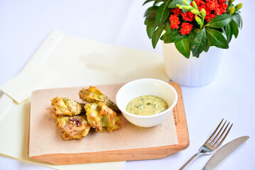 baked zucchini flowers in a white plate on a cutting board with sauce on a white background with a flower