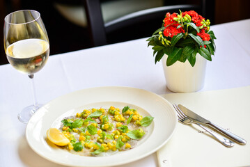 Fish carpaccio decorated with corn and basil on a plate with wine