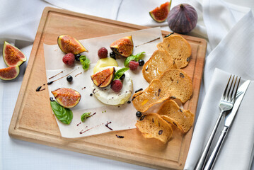 figs drizzled with balsamic sauce on a wooden board with camembert cheese and bruschetta