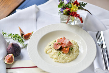 risotto with figs and ham in a white plate on a table with food decor