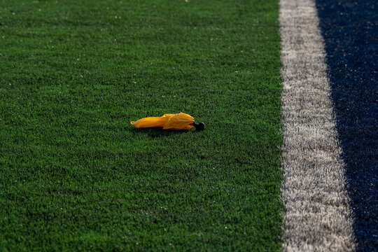 This minimalist photograph captures a bright yellow penalty flag lying on a vibrant green artificial turf sports field. 