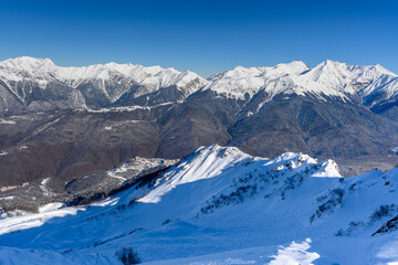 Mountainside, valley. In the background there are beautiful snow-capped mountains and an opening view of the valley. The bright winter sun highlights the snow-white landscapes.