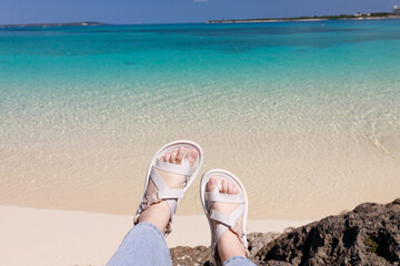Feet with white sandals by emerald beach in Okinawa(沖縄の白砂ビーチと海を背景にした足元の写真）
