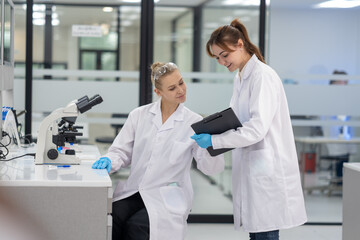 Fototapeta premium Two scientists in white lab coats collaborate on research in a modern laboratory setting during daylight hours