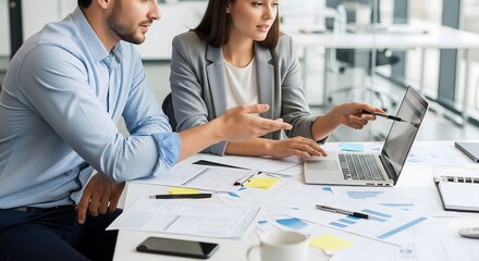 Modern business team collaborating on laptop, reviewing reports in a bright office for effective strategies and innovative solutions