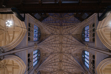 A symmetrical view of a gothic vaulted ceiling with ribbed arches and colorful stained glass windows. The stonework and stained panels reveal intricate craftsmanship inside the cathedral.