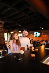 Couple enjoying drinks and snacks at a bar counter, laughing and having fun
