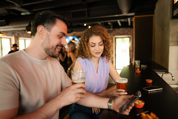 Couple enjoying drinks and using smartphone in pub
