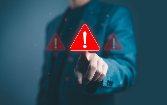 Businessman touching red warning alert icon on virtual screen, symbolizing cybersecurity risk, system error, data protection alert, and online security breach prevention concept in digital technology.