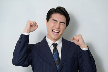 白背景でガッツポーズをするスーツの男性