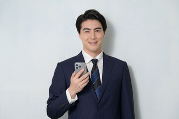 白背景でスマホを持つカメラ目線のスーツの男性