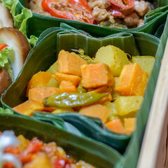 Indonesian acar kuning, yellow pickled vegetables cooked with turmeric and chili, served in banana leaf box. Authentic homemade Asian vegetarian food with eco-friendly packaging
