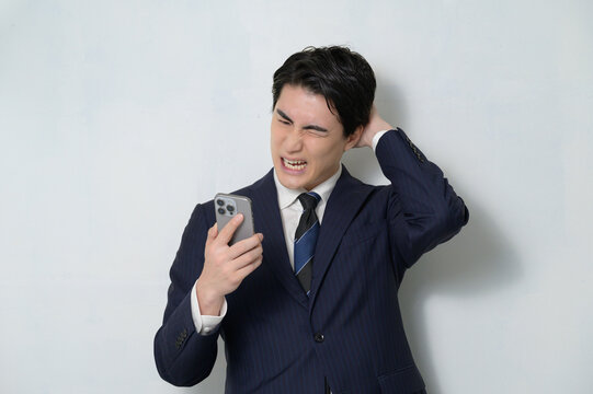 白背景でスーツを着てスマホを見て困る日本人男性