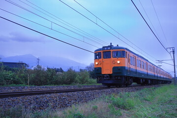 Naklejka premium 浅間山に見守られて曇天の軽井沢を走行するしなの鉄道115系電車(湘南色)_2025/10/4撮影