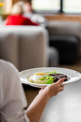 Gourmet steak dish served on a white plate with mashed potatoes and vegetables, held by a person in a restaurant setting. Elegant food presentation for hospitality and culinary themes.