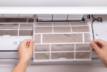 Man hand removing clogged and dirty air filter from home air conditioner. Concept of household hygiene, dust pollution and home air quality.