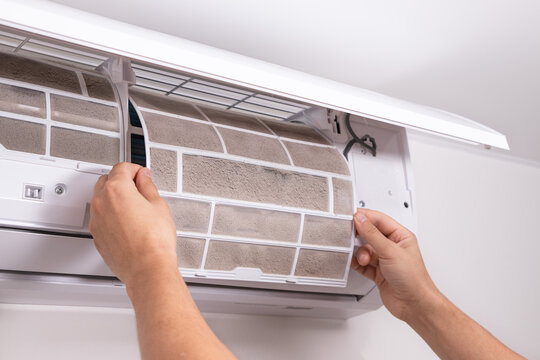 Man hand removing clogged air conditioner filter covered in dust and dirt. Concept of dirty indoor air, air purification, regular AC maintenance, and household hygiene.