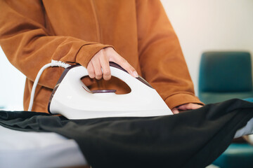 Woman Using Modern Iron on Black Fabric in Bright Room with Natural Light and Fashionable Background Elements
