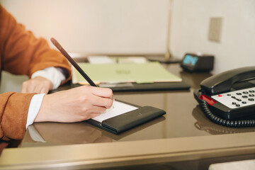 Person Writing on Notepad with Pen at a Desk with Telephone and Folders in a Modern Office...