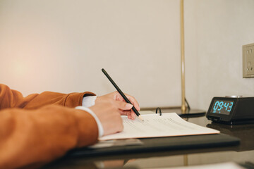 Fototapeta premium Person Writing Notes on Paper with Clock in Background in Modern Workspace Setting