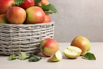 Fresh ripe apples with green leaves in wicker basket on white wooden table, closeup