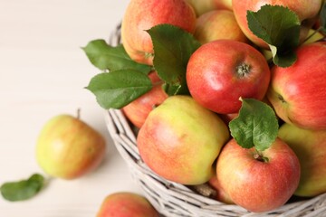 Fresh ripe apples with green leaves in wicker basket on white table, closeup