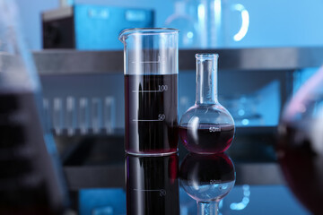 Glass beaker and flask with red liquid on table in laboratory, selective focus