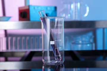 Glass beaker and test tube with red liquid on table in laboratory, closeup