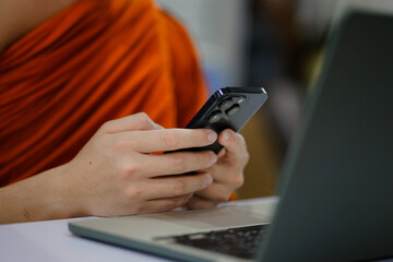 Monks and priests, men in orange robes, use smartphones with white screens.