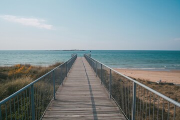 Obraz premium A walkway featuring metal handrails guides you to the dock and the campfire area, with some sandy shore and sea visible on the right side.