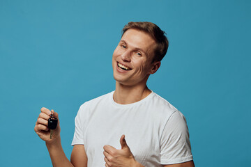 smiling young caucasian man hold car keys show thumbs up gesture wear white t-shirt blue background digital detox concept