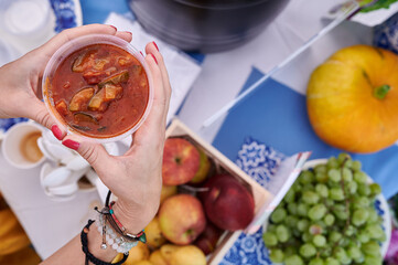 Hand holding glass of tomato soup over colorful market table with fruits and vegetables, Wloclawek, Poland, top view, bright natural light, food photography.