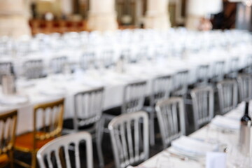 Blurry fine dinning setup of chairs, long tables with tablecloths, plates, cutlery and glasses. Wide angle, interior setting, top down, no people