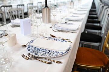 Empty, delft blue decorated ceramic dinner plate and silver cutlery arranged on a white table cloth. Top side view, shallow depth of field, no people