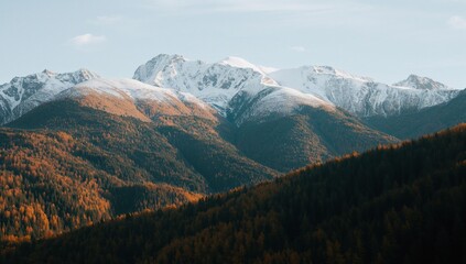 Obraz premium Autumnal landscape of snowy mountain peaks and vibrant mixed forests at their base