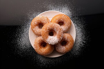 Sugary donuts dusted with powdered sugar on a dark surface. Culinary theme. Empty area for text.