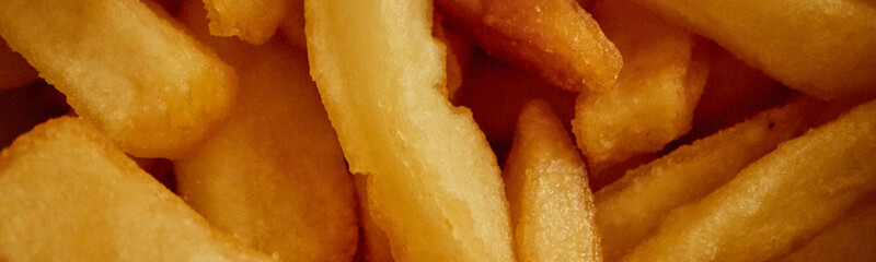 Website header shot of golden fried potato fries stacked together, crispy texture visible on surface, no people present, emphasizing detail of cooked food, suitable for culinary or snack concepts